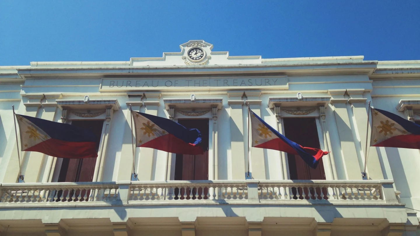 Philippine flags hanging from the balcony of the Bureau of the Treasury building in Manila under a clear blue sky