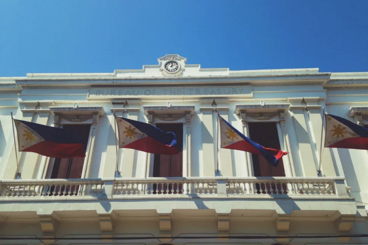 Philippine flags hanging from the balcony of the Bureau of the Treasury building in Manila under a clear blue sky