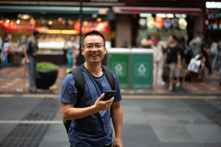 Smiling man holding a smartphone on a city street