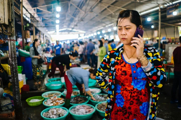 Market vendor checking her phone at a busy wet market